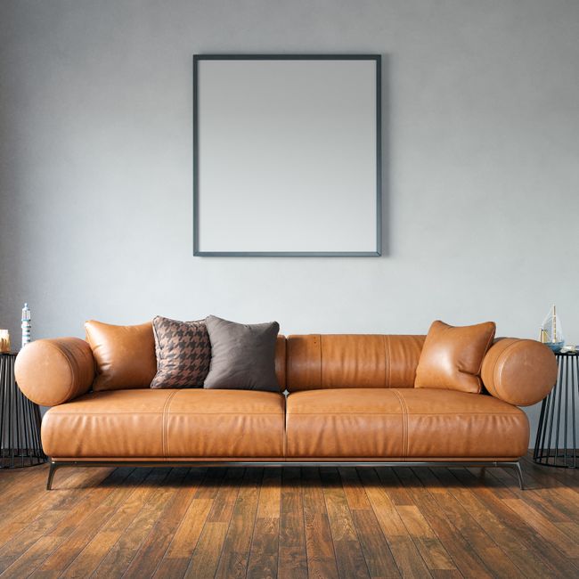 A white upholstered sofa with tufted detailing on the backrest and rolled arms, positioned against a white paneled wall in a well-lit room. The sofa is clean, with smooth fabric cushions, and sits on dark wooden legs on a parquet wooden floor. There are no visible stains or dust, indicating recent surface cleaning or maintenance by Belgravia Carpet Cleaning, supporting their domestic cleaning and surface sanitisation services.